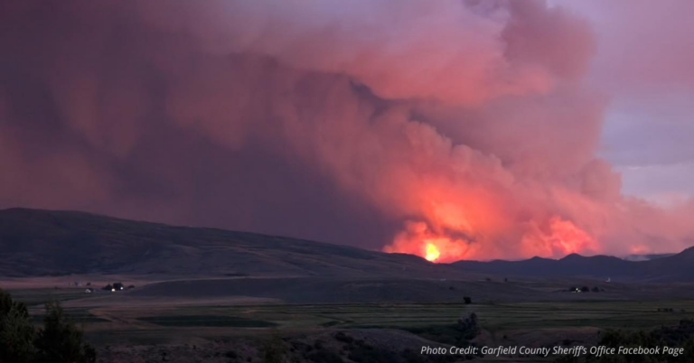 Massive wildfire glows at dusk behind rolling hills near Meeker