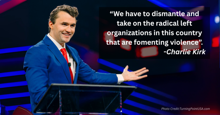 Charlie Kirk onstage with outstretched arm smiling