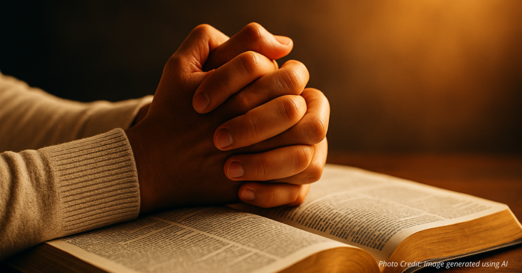 Hands clasped in prayer over an open Bible with golden light