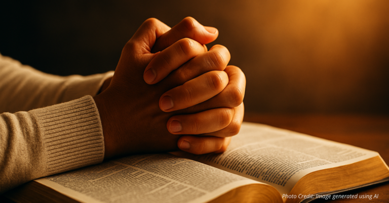 Hands clasped in prayer over an open Bible with golden light