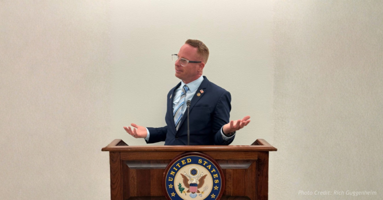 Rich Guggenheim stands at a podium, gesturing as he speaks during a public appearance.