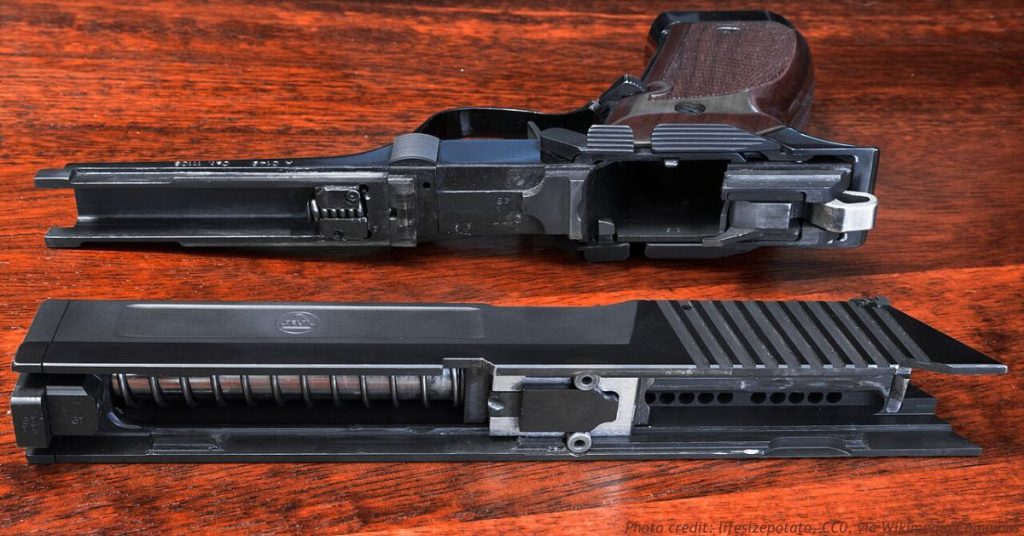 Field-stripped semi-automatic pistol laid out on a wood surface, frame and slide with recoil spring separated.
