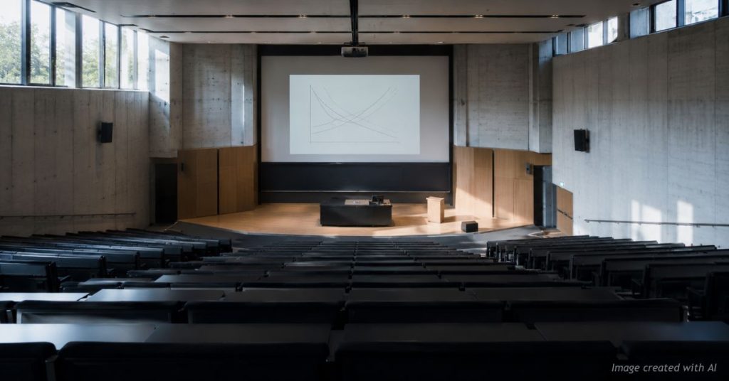 Empty university lecture hall with faint economics supply and demand curves on the projection screen, no students present.