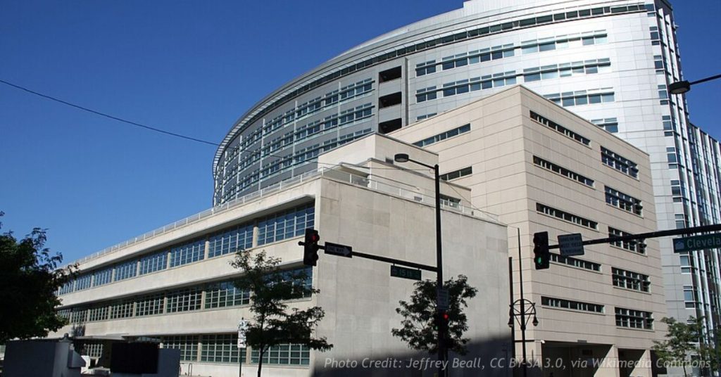 The Wellington E. Webb Municipal Office Building in downtown Denver, a limestone office block with a curved glass tower rising behind it, seen from the corner of 15th Street and Cleveland Place.