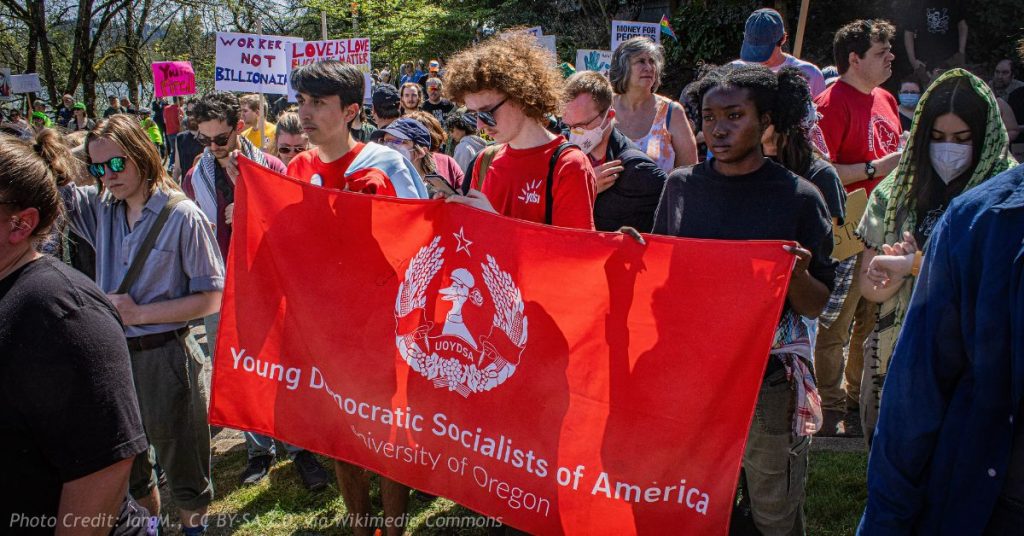 Students hold a red Young Democratic Socialists of America, University of Oregon banner at an outdoor rally.