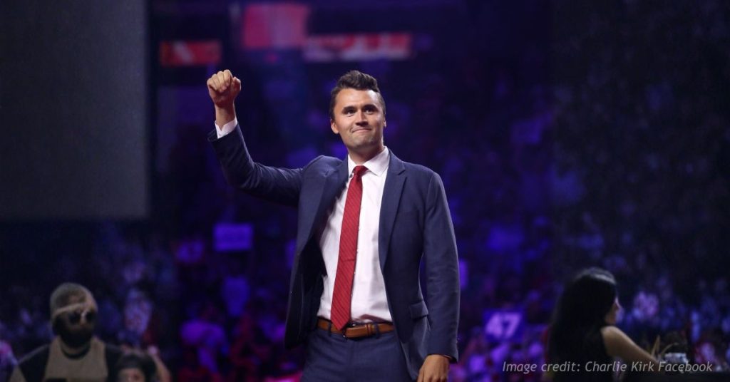 Charlie Kirk raises his fist while appearing onstage at a public event.