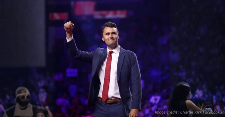 Charlie Kirk raises his fist while appearing onstage at a public event.