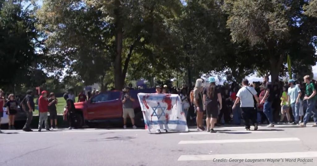 Protesters at Denver's La Alma park ICE walkout hold an Israeli flag marked with red handprints in a crosswalk.