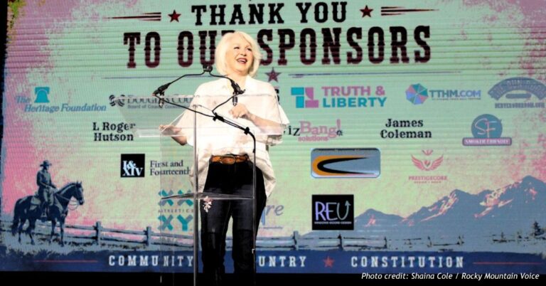 Tina Peters speaks behind a clear podium at Freedom Fest, with a Rocky Mountain Voice sponsor acknowledgment displayed on the screen behind her.