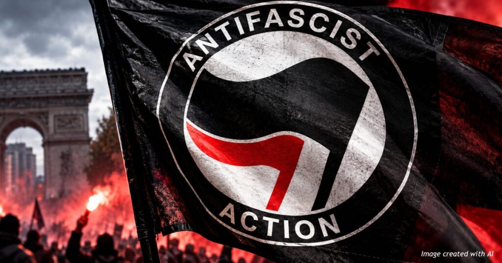 Black flag displaying the red, white and black Antifascist Action emblem against a smoky Paris protest scene, with the Arc de Triomphe in the background.