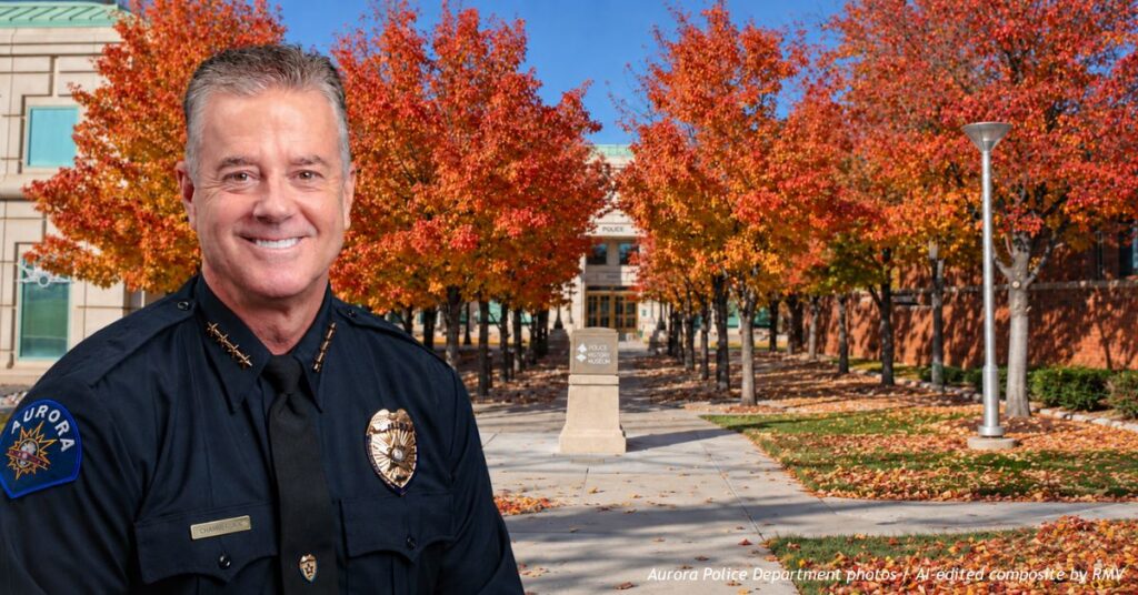 Aurora Police Chief Todd Chamberlain in uniform, with Aurora Police Headquarters and autumn-colored trees in the background.